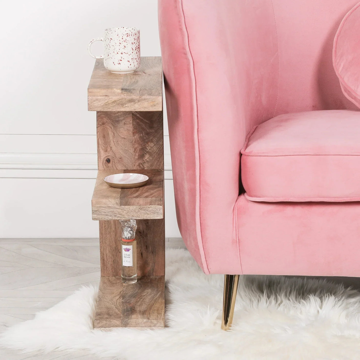 Wooden side table with shelves beside pink sofa on white rug, holding mug and decor