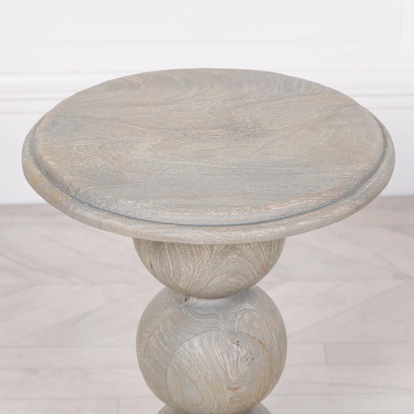 Round wooden side table with sculpted spherical base on light wood floor