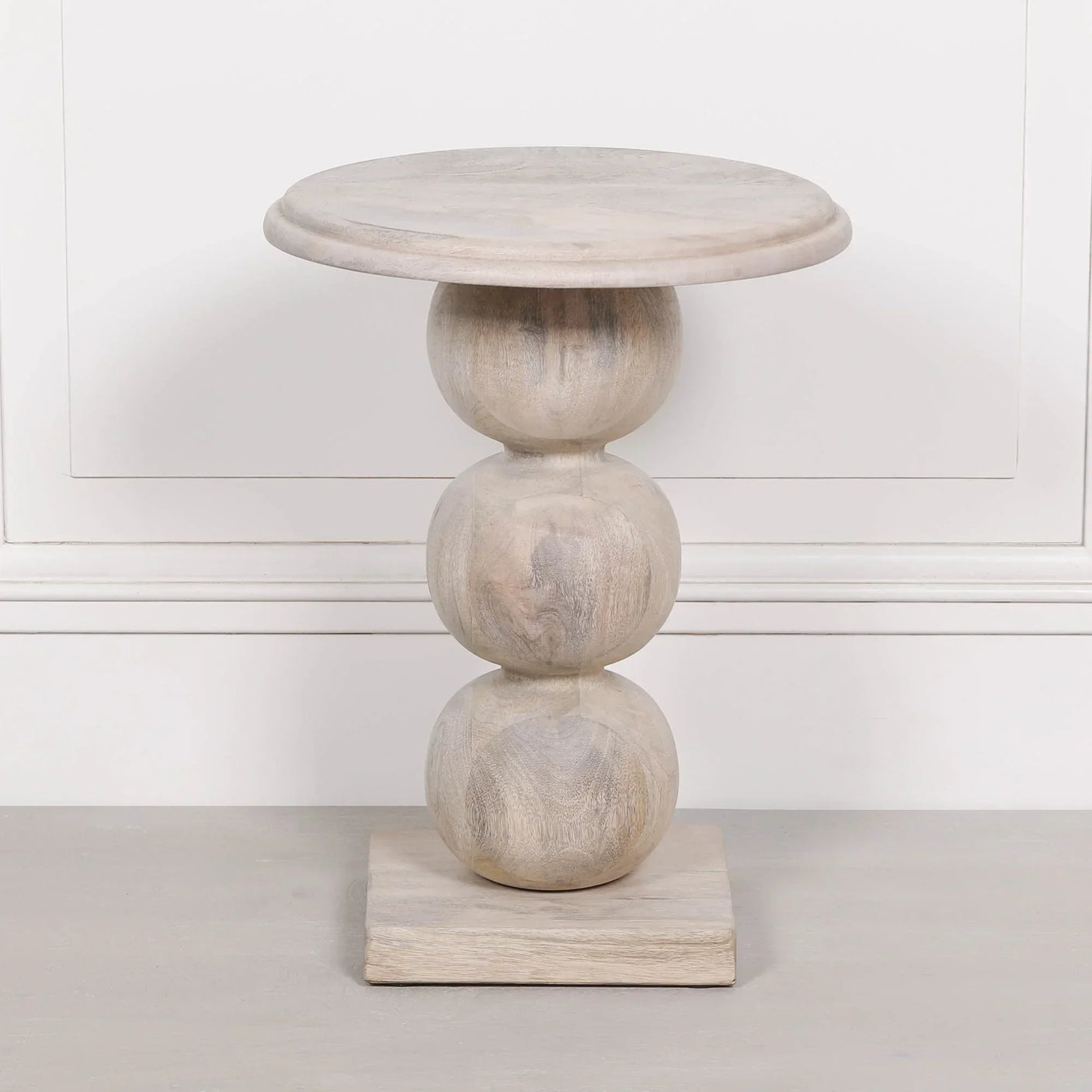 Light wood side table with three stacked globe base and round top against white wall