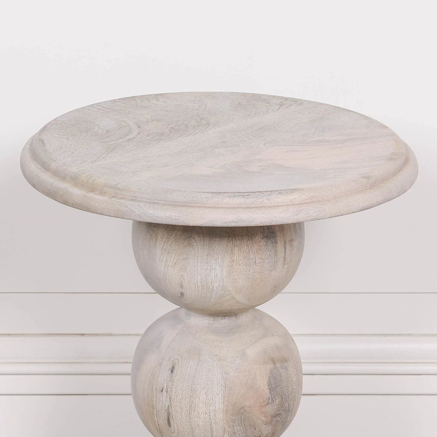 Round wooden side table with natural finish and sculpted base against white wall