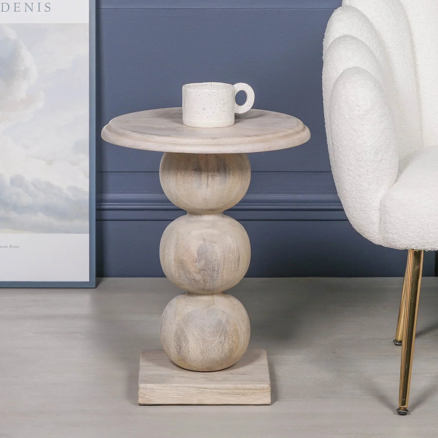 Round wooden side table with sculpted spherical base next to a white accent chair