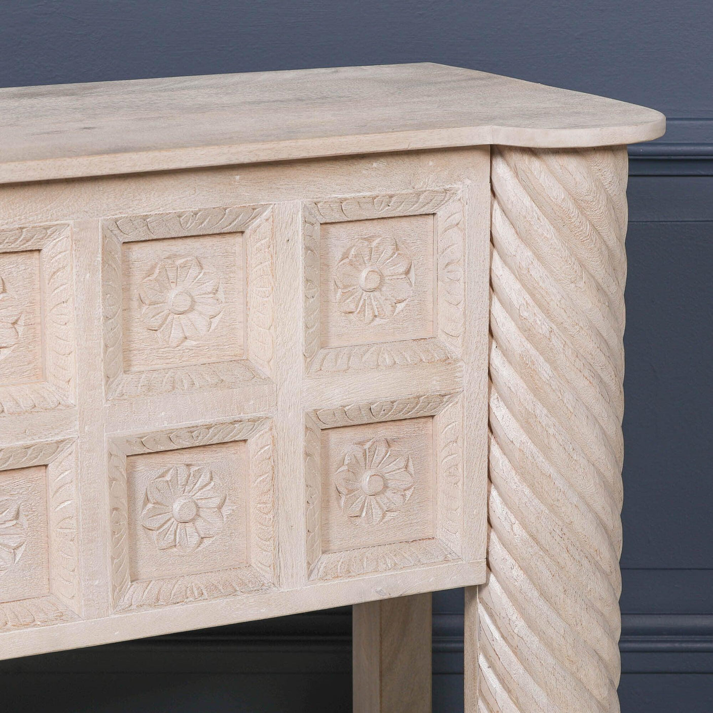 Carved wood console table with floral panel detail and twisted leg against grey wall