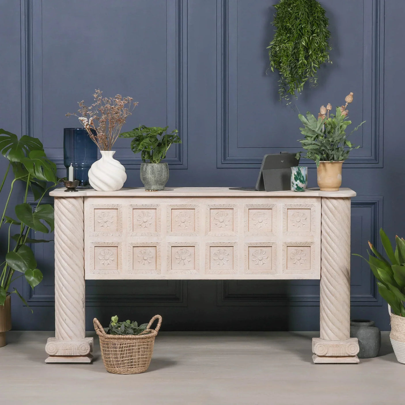 Carved wood console table with floral panels and twisted columns, styled with potted plants