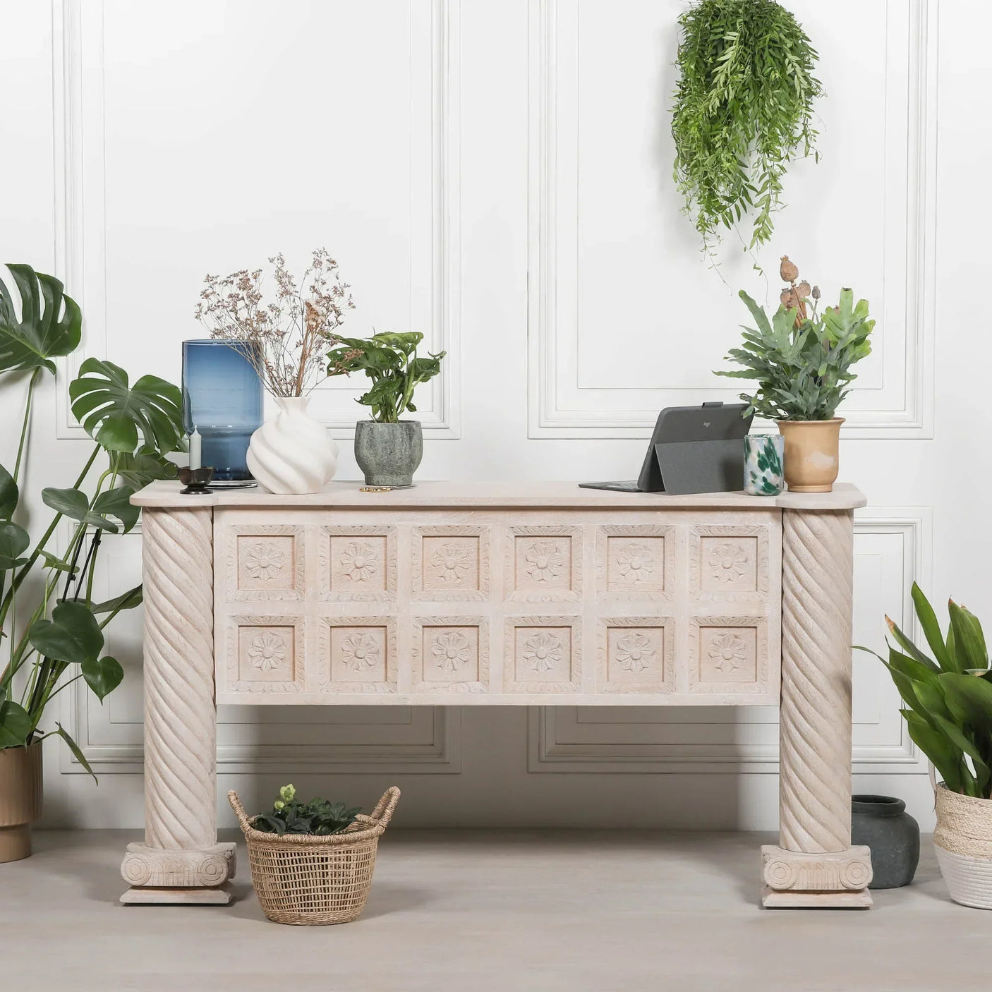 Carved wooden console table with floral panels and twisted columns, styled with plants and vases