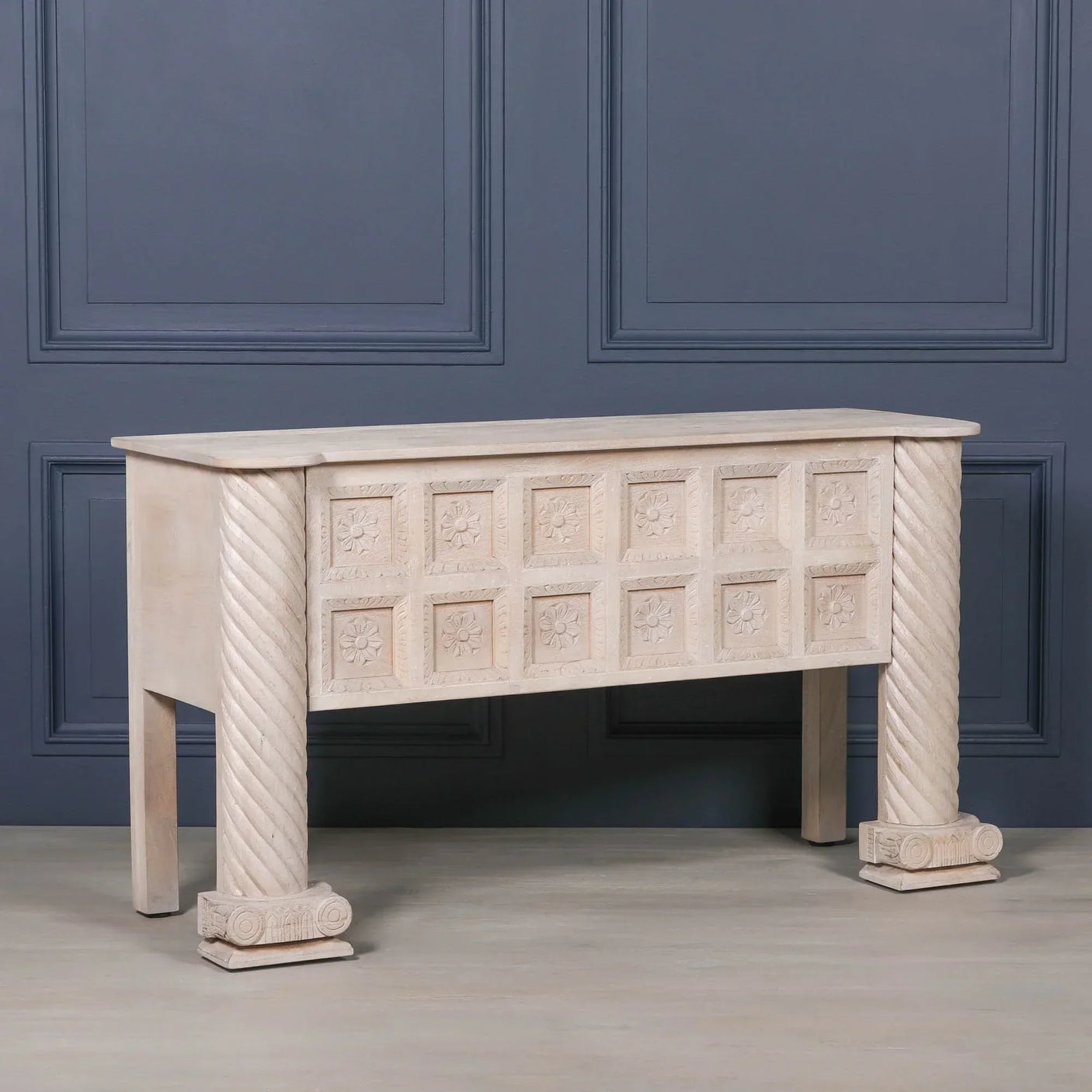 Carved wooden console table with twisted legs and floral pattern front against blue wall