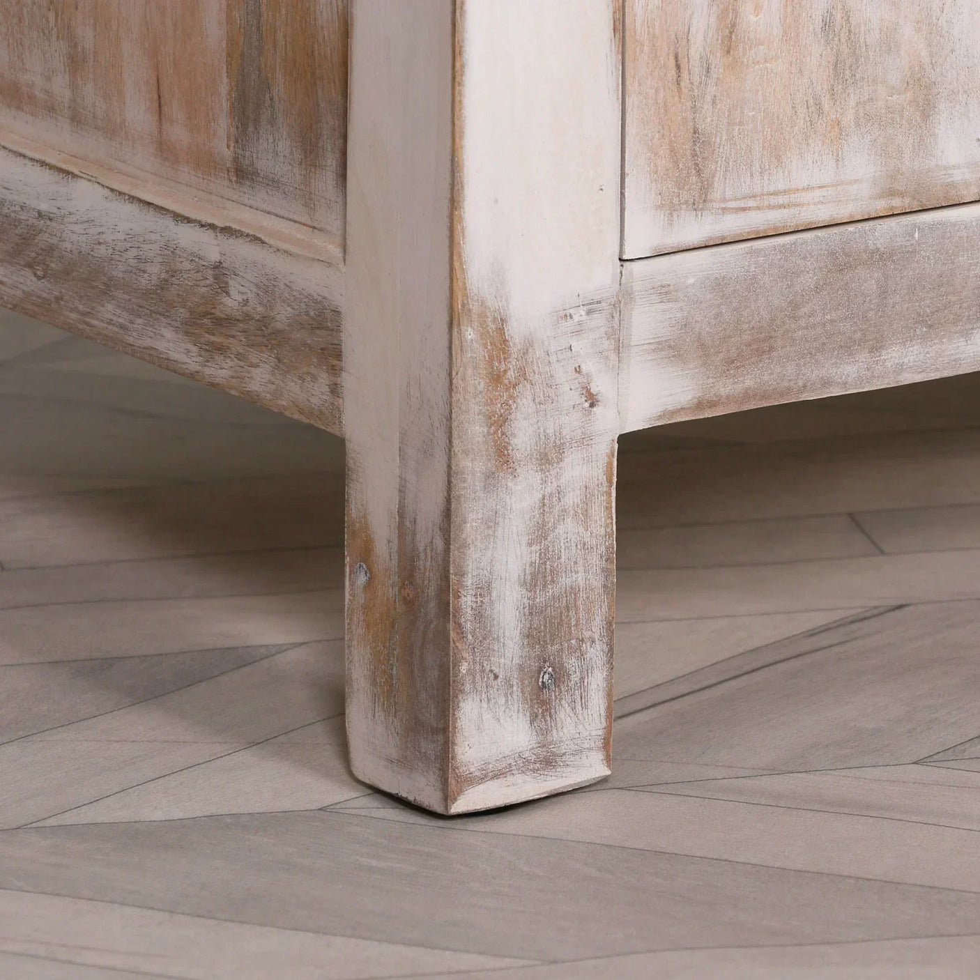 Distressed wood furniture leg with whitewashed finish on chevron parquet flooring