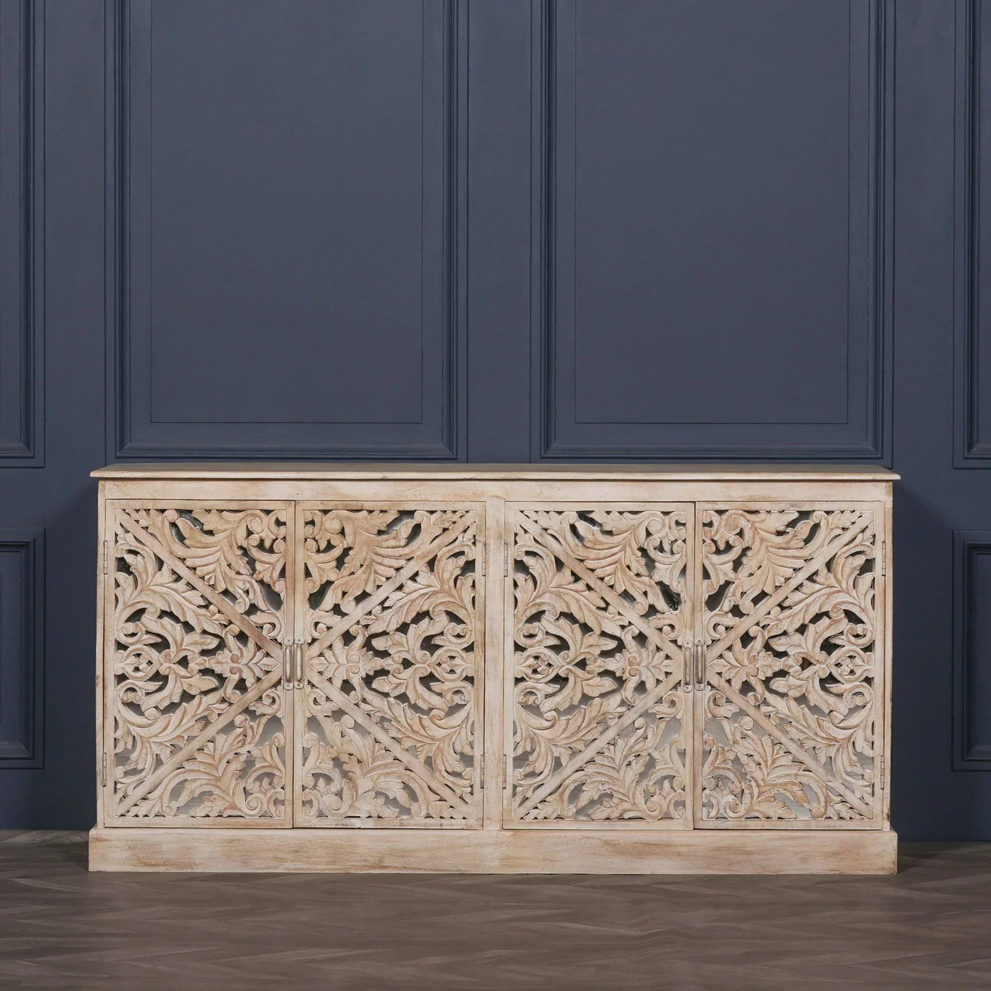 Carved wood sideboard with ornate floral patterns and light distressed finish against navy wall