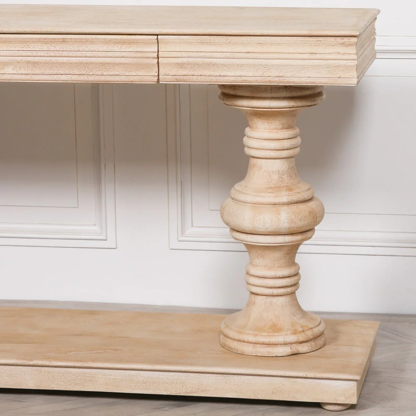 Beige wood console table with turned pedestal base and lower shelf against white wall