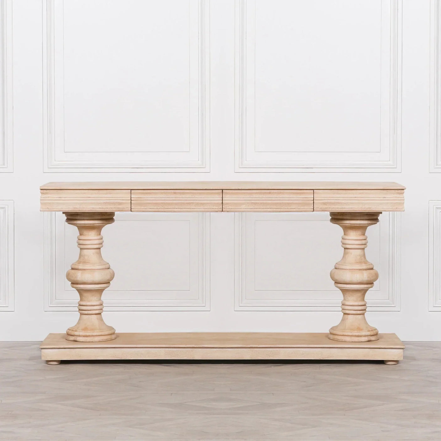 Light wood console table with carved pillar legs and lower shelf against white panel wall