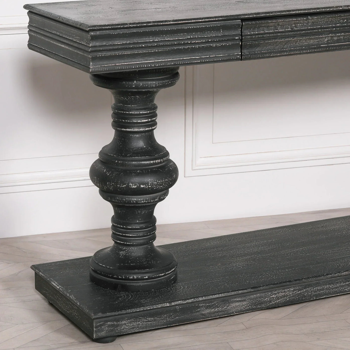 Black wood console table with ornate turned leg and distressed finish on hardwood floor