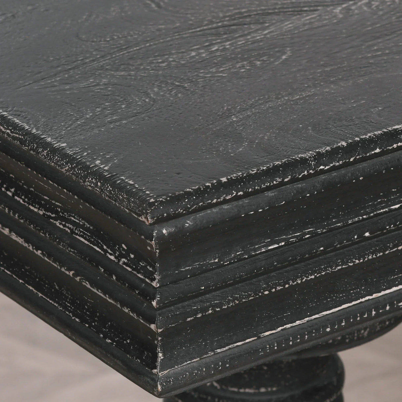 Distressed black wooden dining table corner with textured grain and layered edge detail