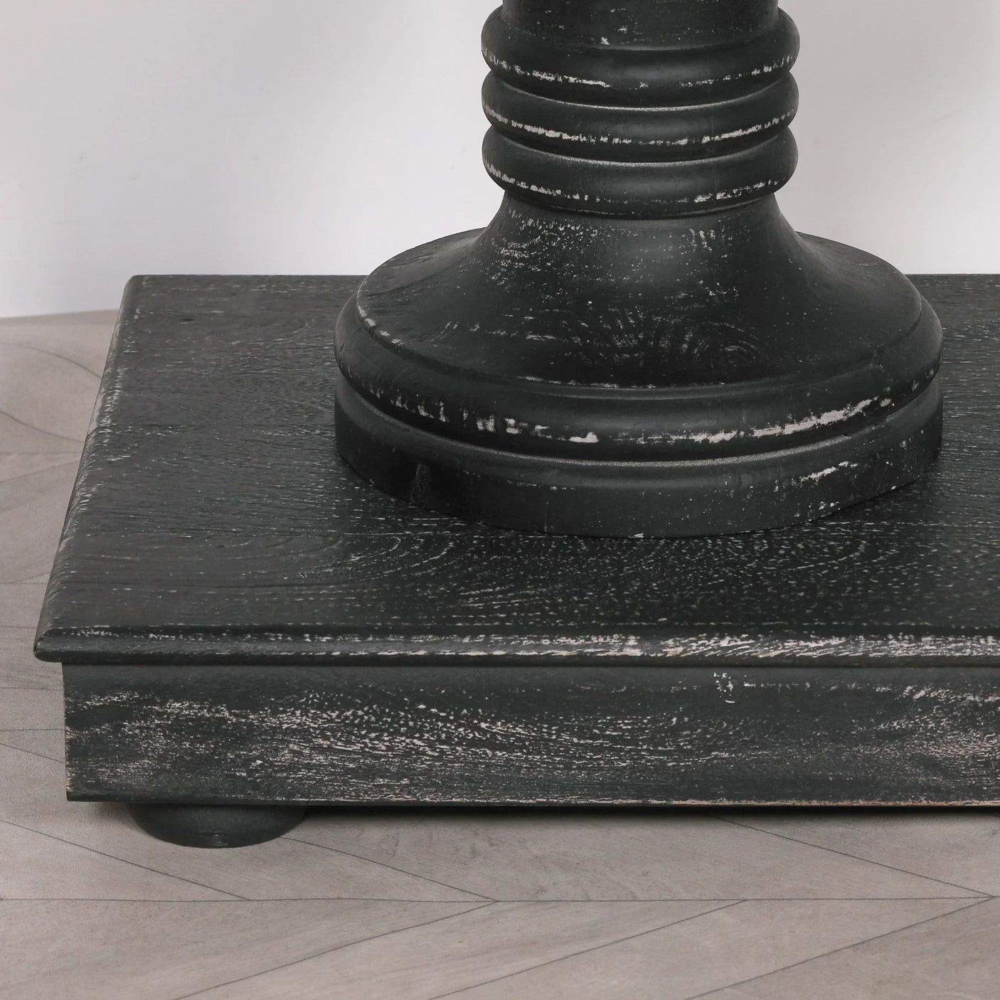 Close-up of black wooden dining table pedestal base with distressed finish on parquet floor