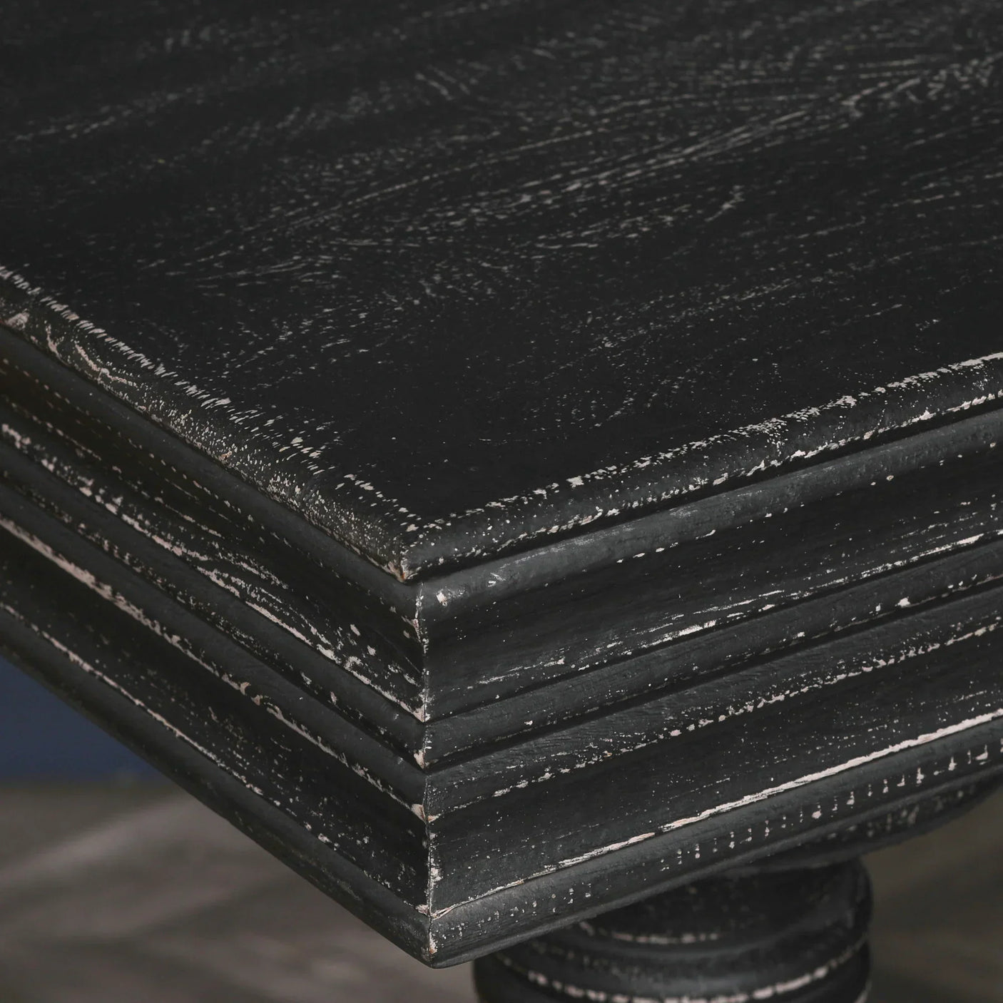 Distressed black wood dining table corner with visible grain and layered edge detail