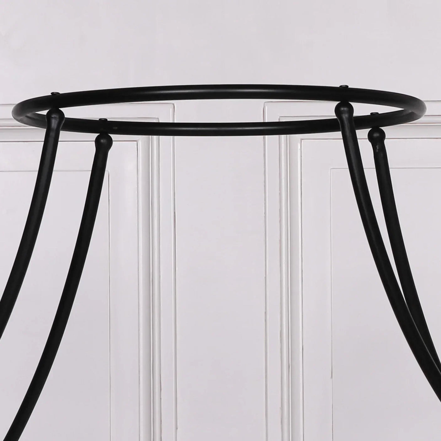 Black metal table base with round frame and curved legs against white paneled wall