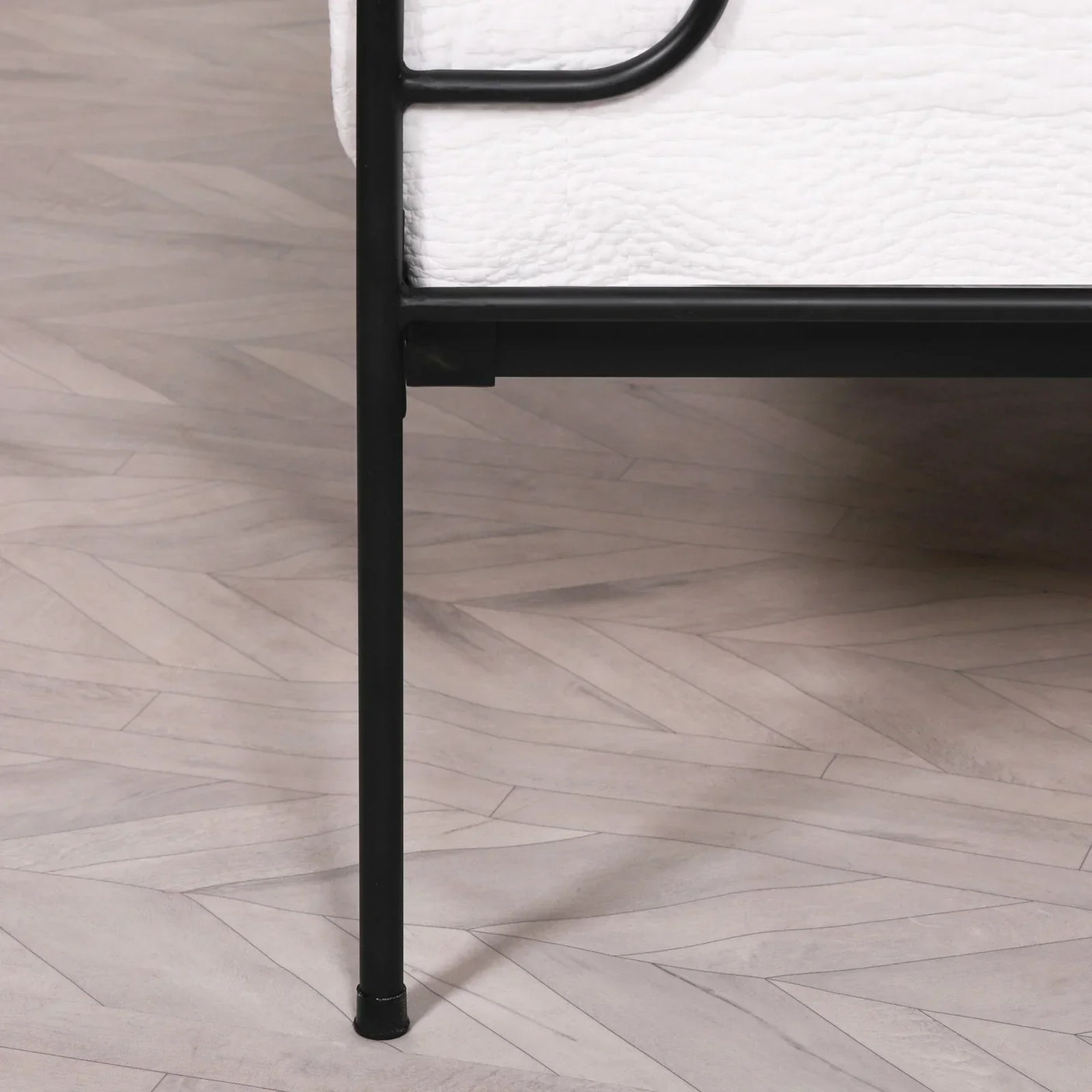 Black metal bed frame leg and white mattress on light herringbone wood floor