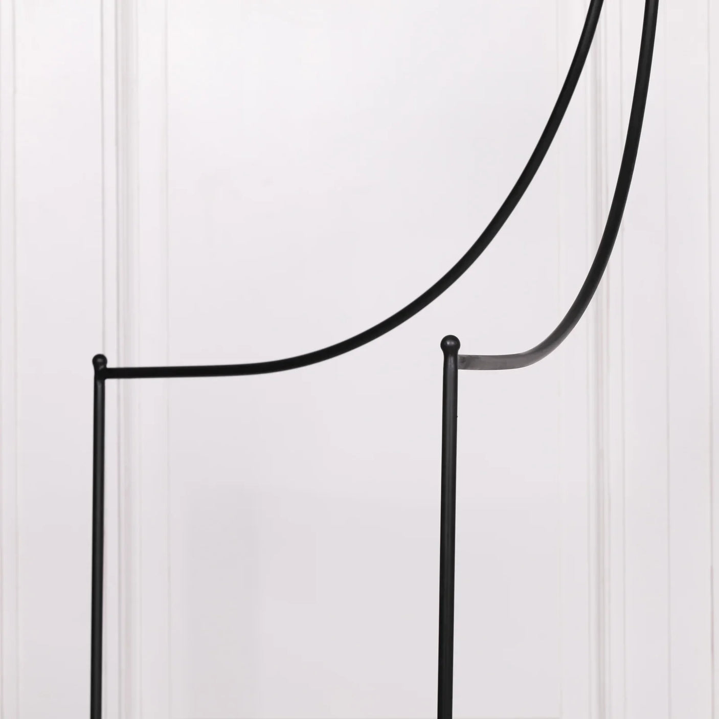 Minimalist metal chair frame in black against white panel wall, side profile view