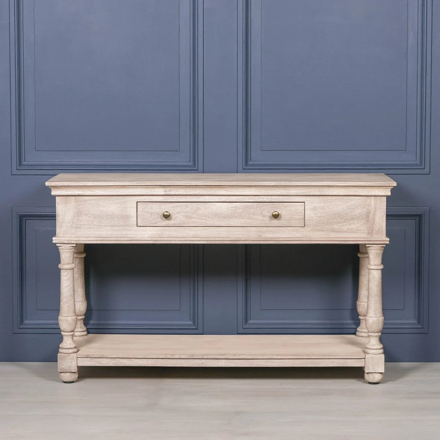 Light wood console table with one drawer, shelf, and turned legs against blue wall