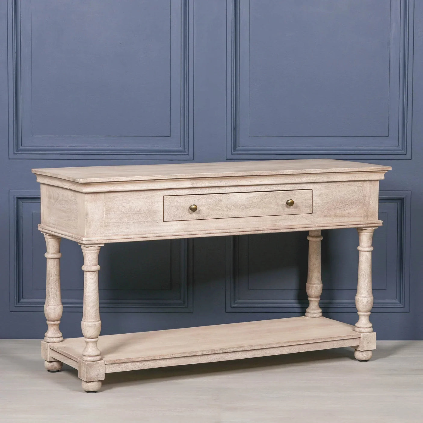 Light wood console table with drawer and lower shelf against blue paneled wall