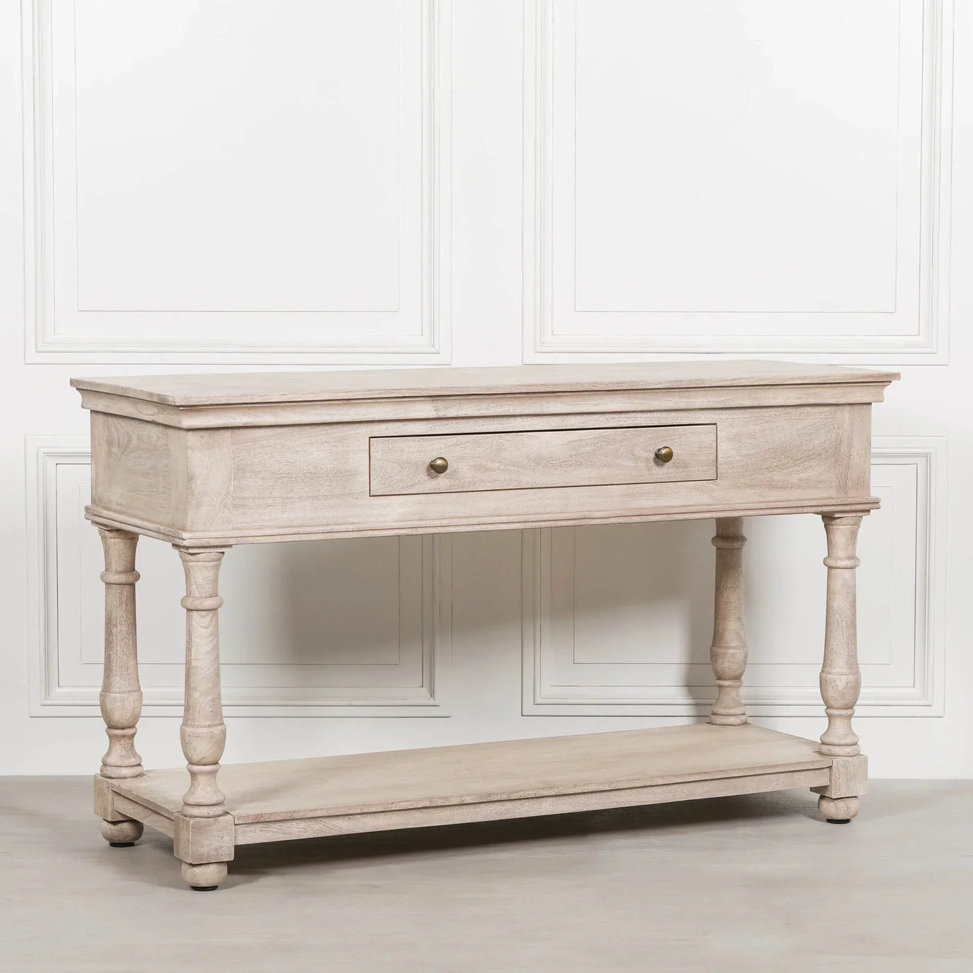 Light wood console table with drawer, turned legs, and lower shelf against white panel wall
