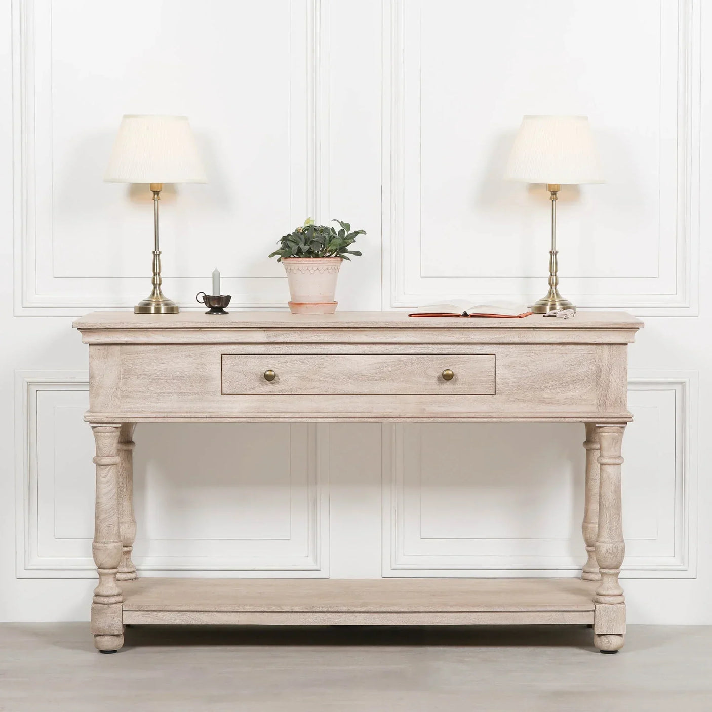 Light oak console table with drawer, two brass lamps, potted plant, and book in hallway