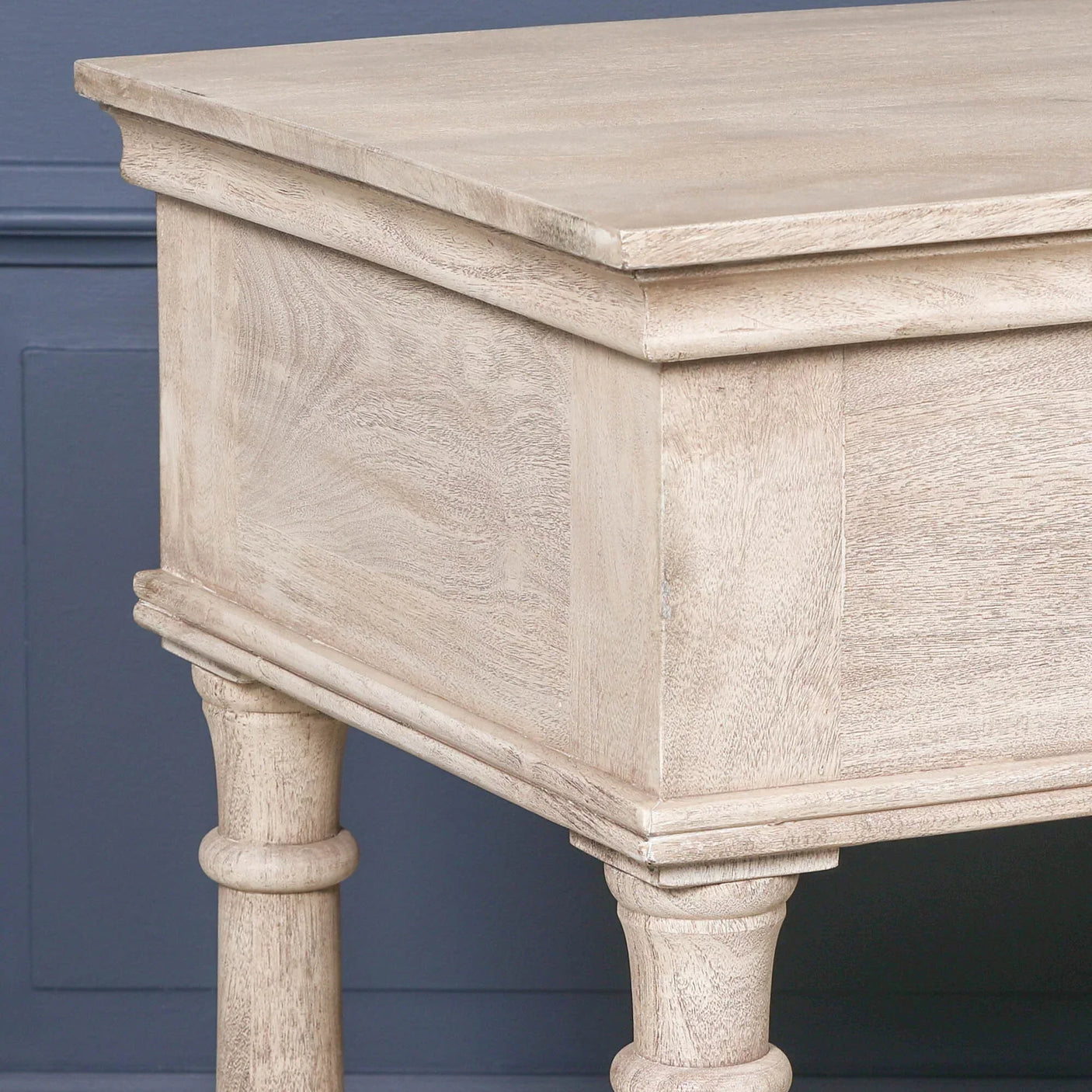 Light wood console table with carved legs and rectangular top against blue wall