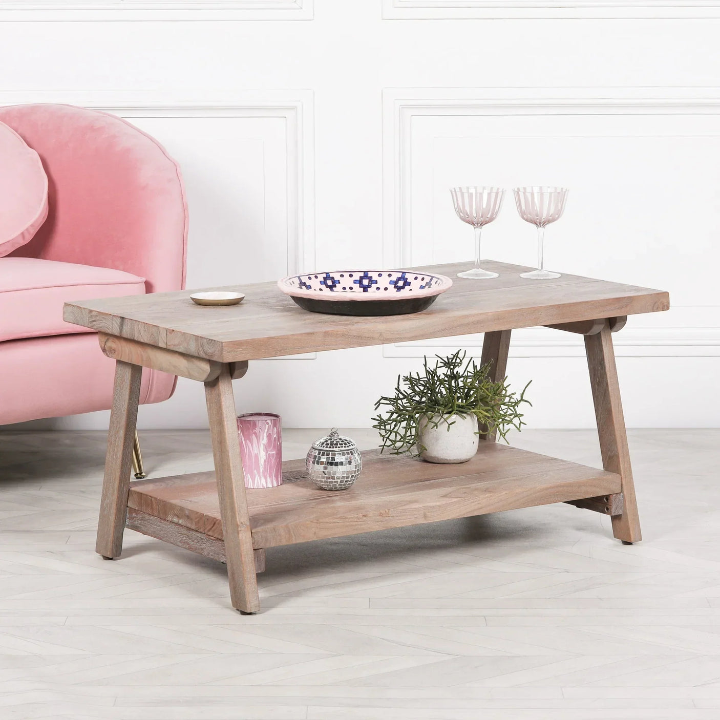 Wooden coffee table with lower shelf, decorative bowl, glasses, and plant in modern living room