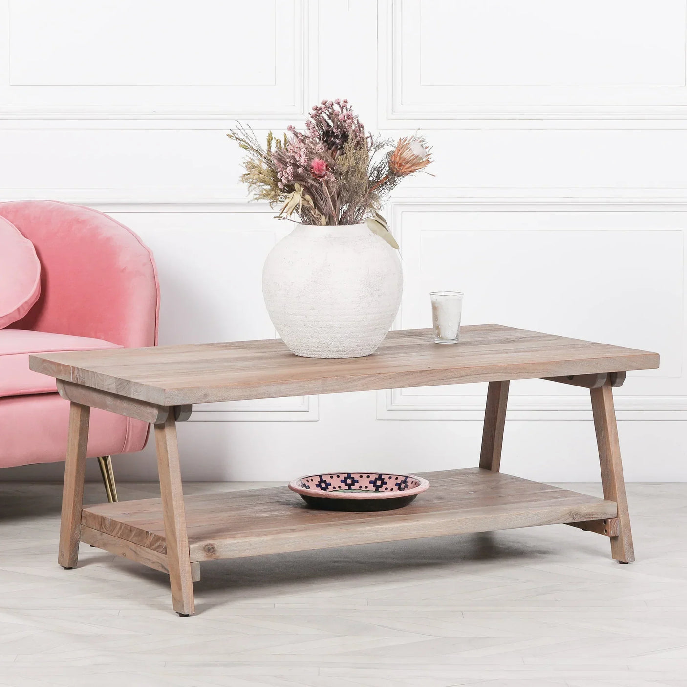 Rustic wooden coffee table with shelf, white vase and dried flowers, pink armchair beside