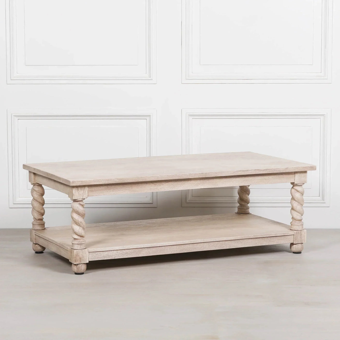 Light oak coffee table with twisted legs and lower shelf against white panel wall