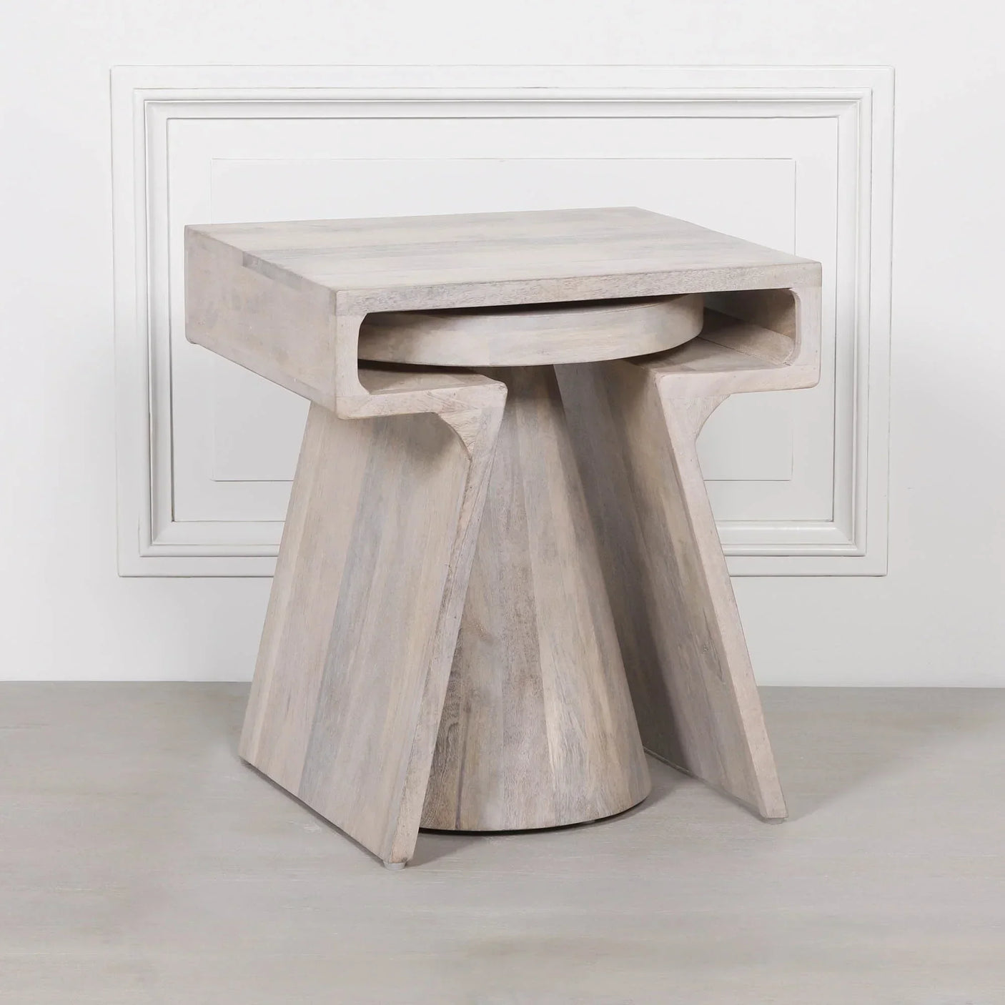 Light wood side table with geometric base and square top against white wall