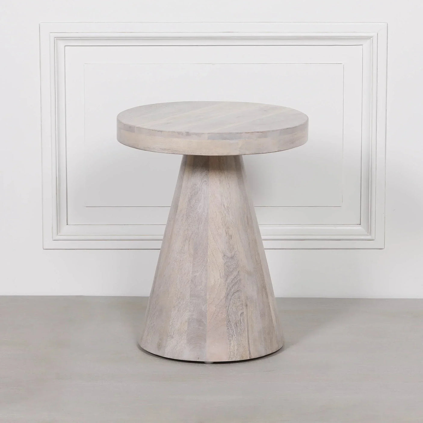 Light wood side table with round top and conical base against a white panelled wall