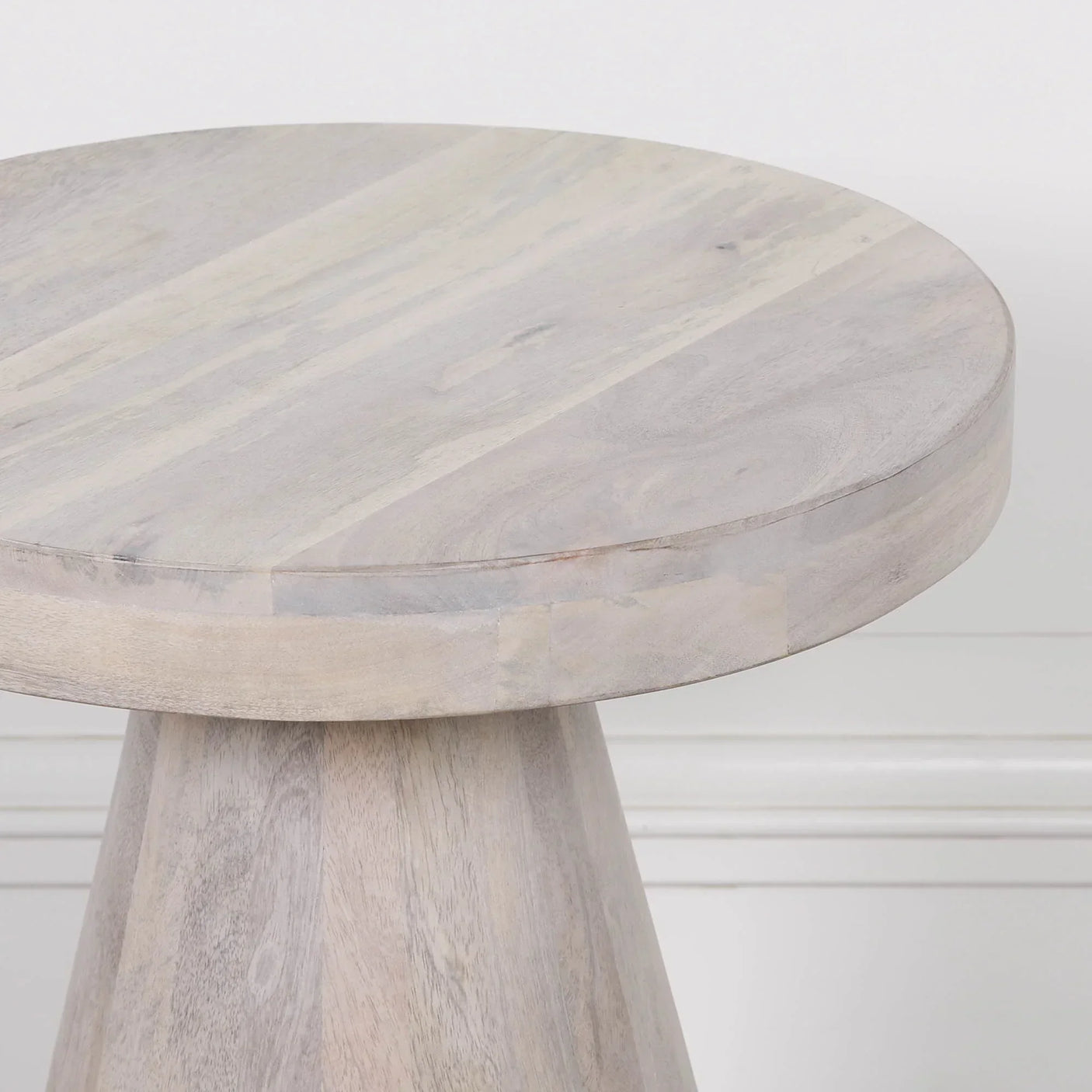 Round light wood side table with conical base against white wall