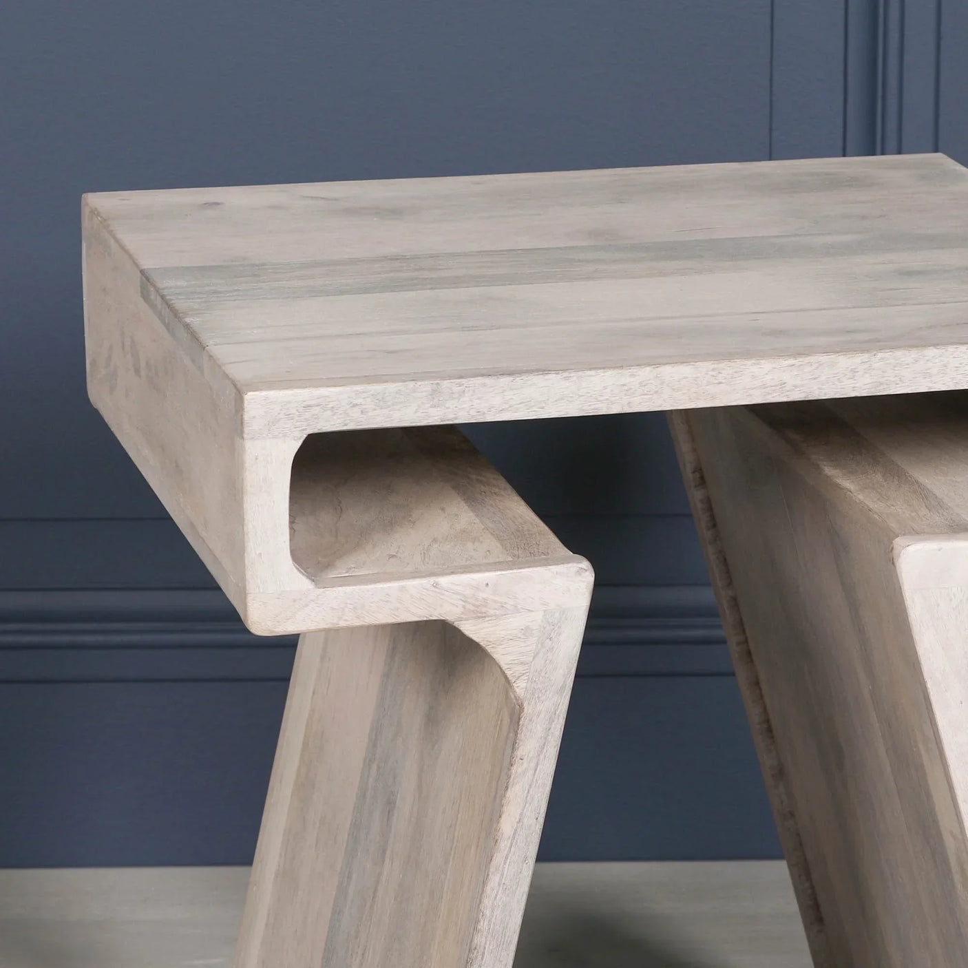 Light wood side table with angled legs and modern geometric design against a blue wall