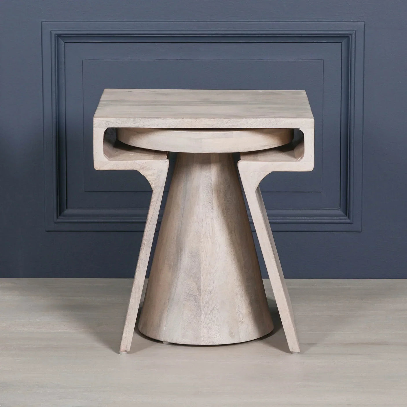 Light wood side table with geometric design and natural finish against blue wall panel