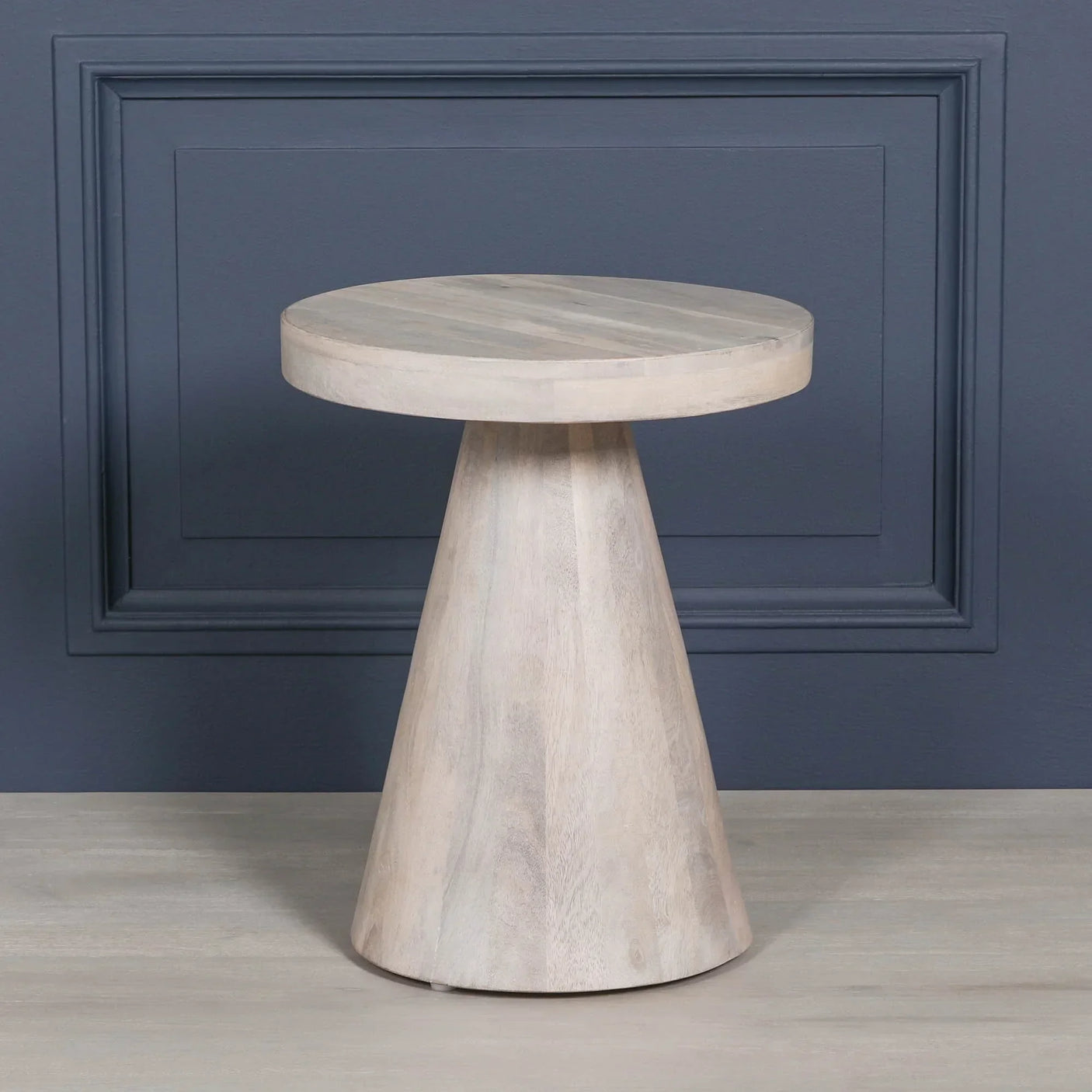 Round wooden side table with conical base in light finish against dark wall