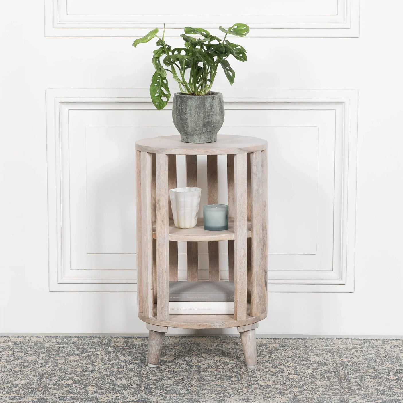 Round wooden side table with slatted design, indoor plant, candles, and books