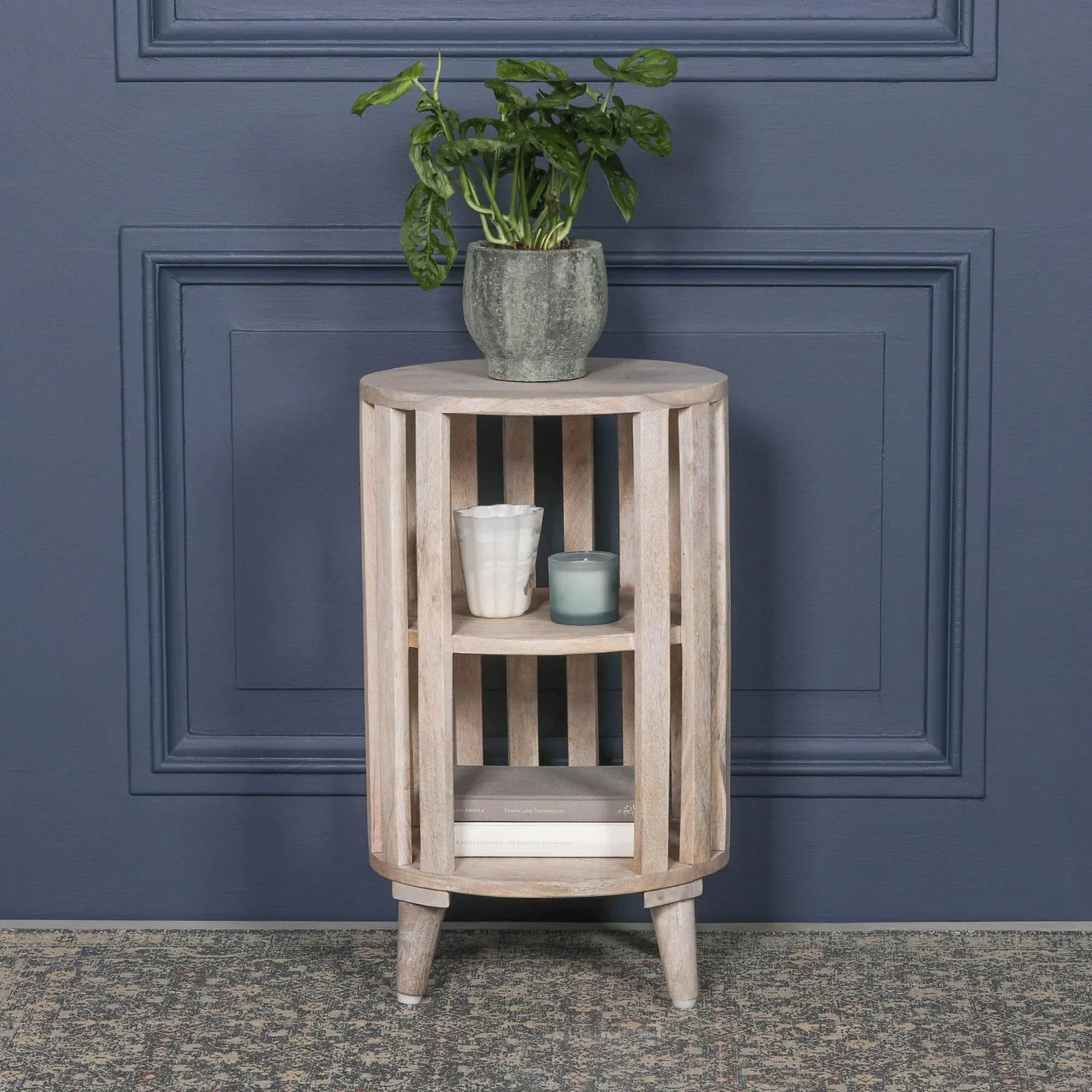 Wooden side table with slatted design, shelves, potted plant, candles, and books