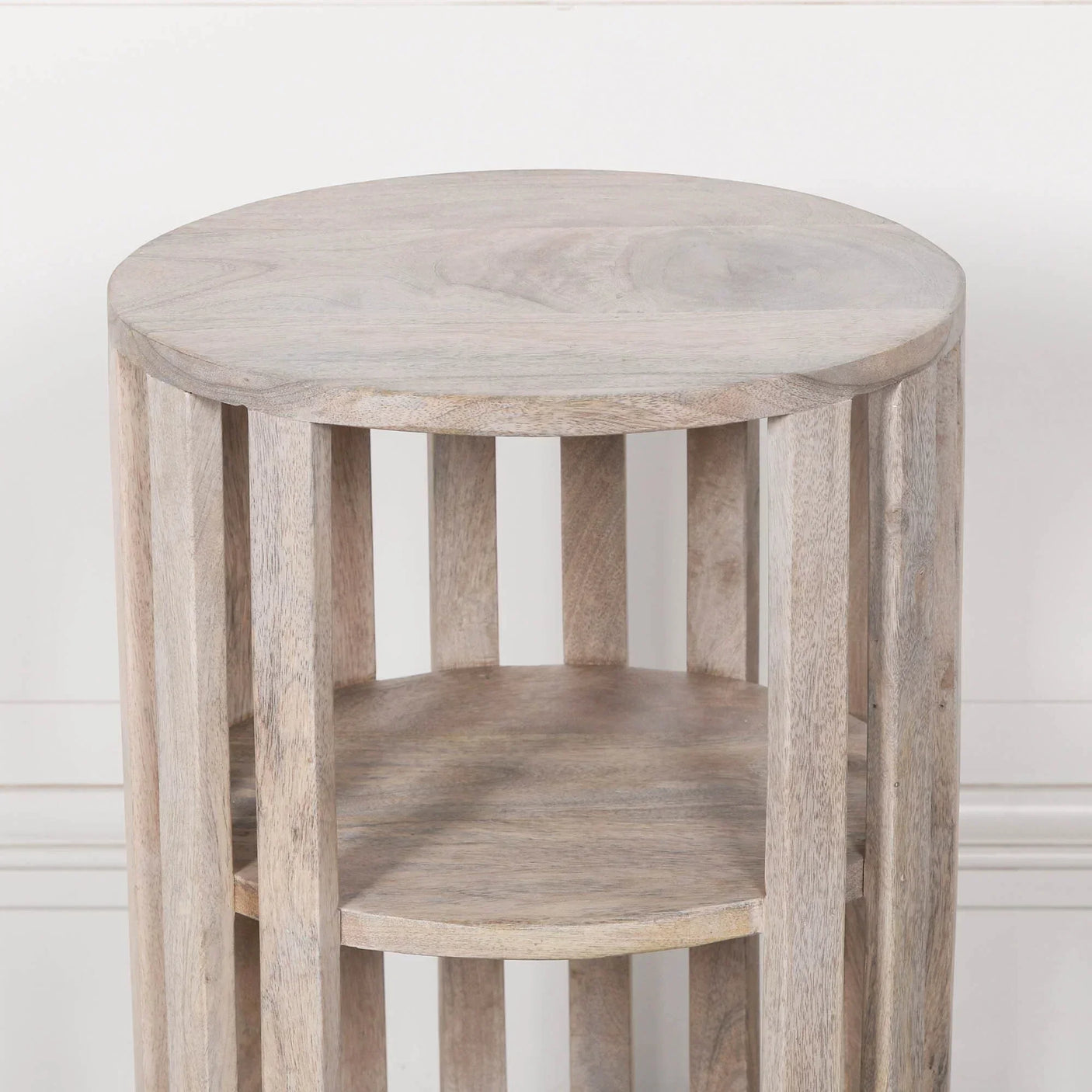 Light wood round side table with slatted base and two shelves against white wall