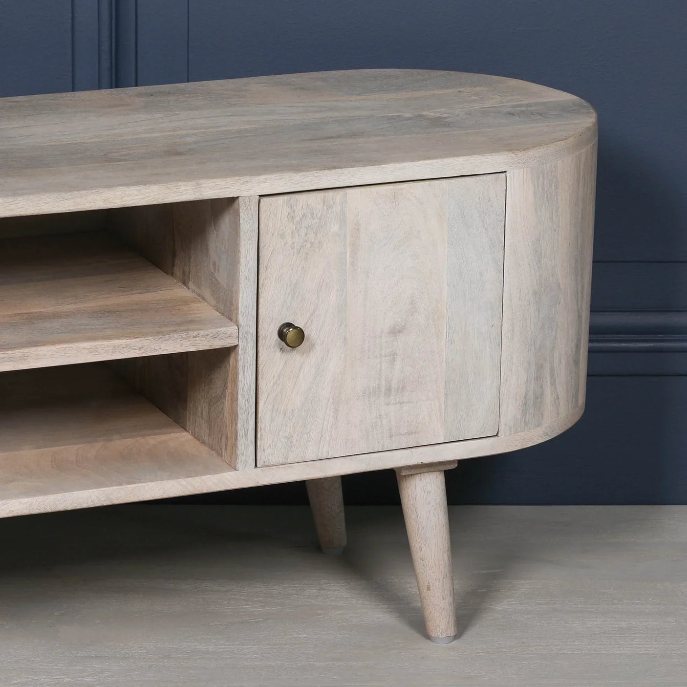 Light wood TV unit with open shelves and single cabinet door, angled legs on timber floor