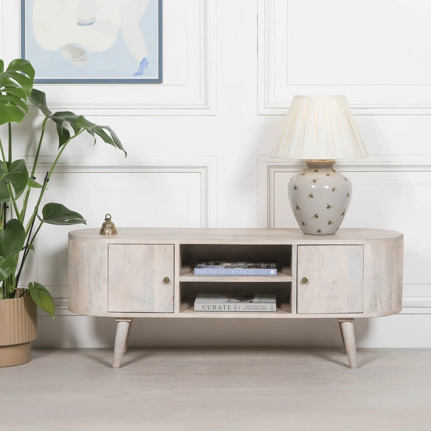 Light wood TV stand with two doors, open shelves, ceramic lamp and books, modern living room
