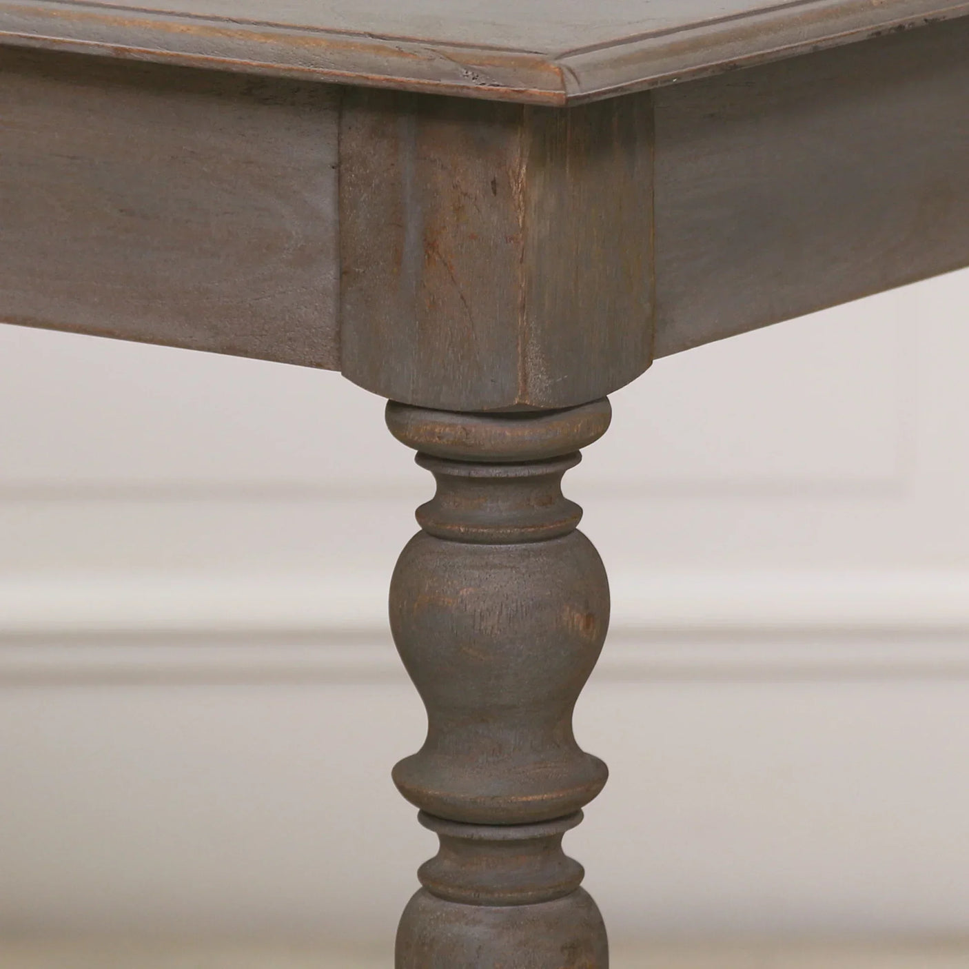 Close-up of wooden dining table corner with turned leg and rustic brown finish