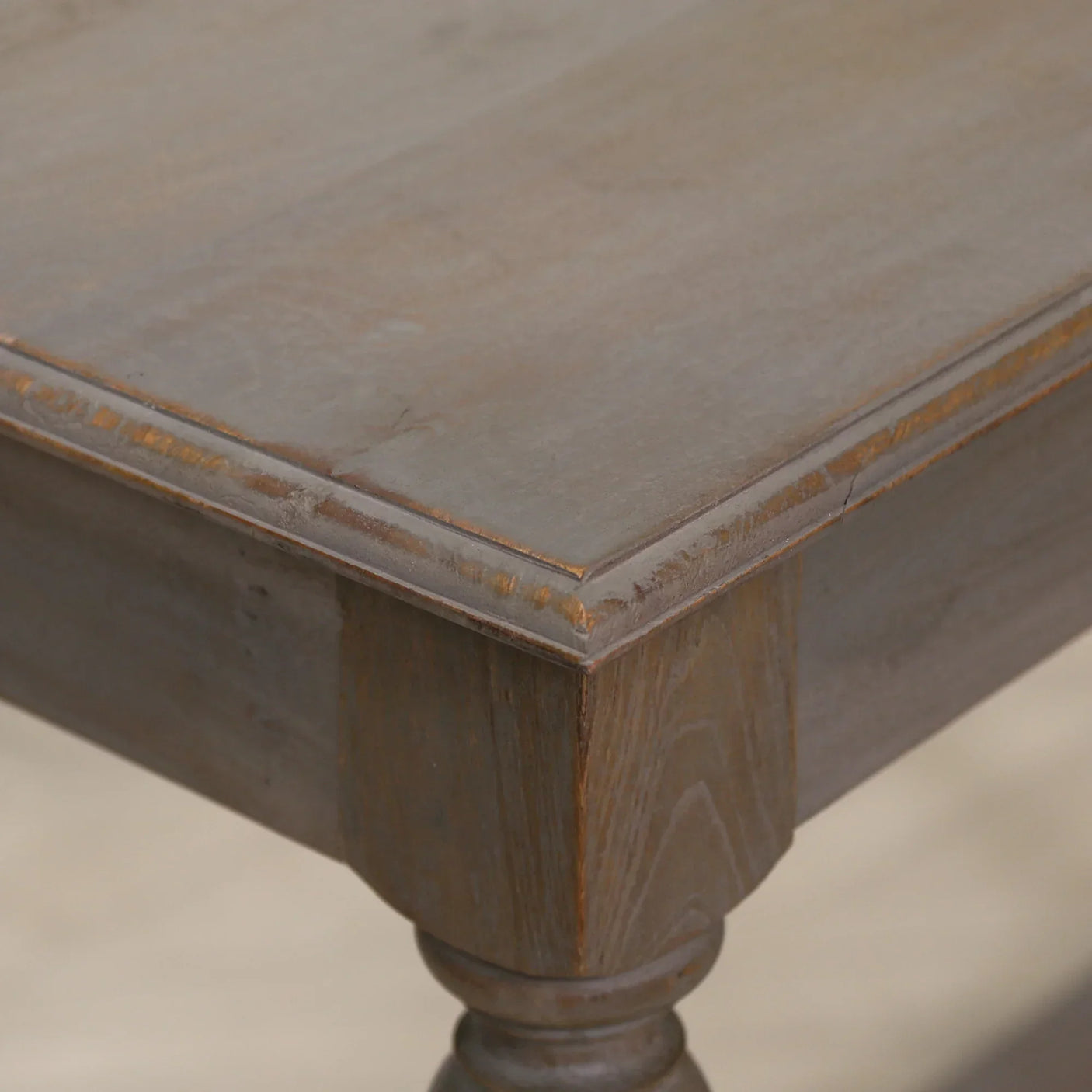 Close-up of rustic wooden dining table corner with visible grain and turned leg detail