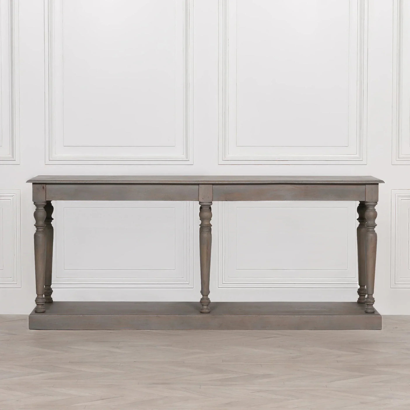 Grey wooden console table with turned legs, rectangular top and bottom shelf against white wall