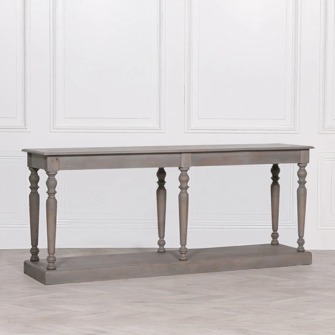 Grey wooden console table with turned legs and bottom shelf against white wall