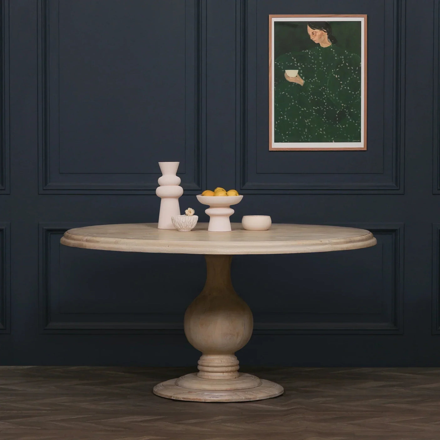 Round wooden dining table with pedestal base, styled with ceramics against dark panel wall
