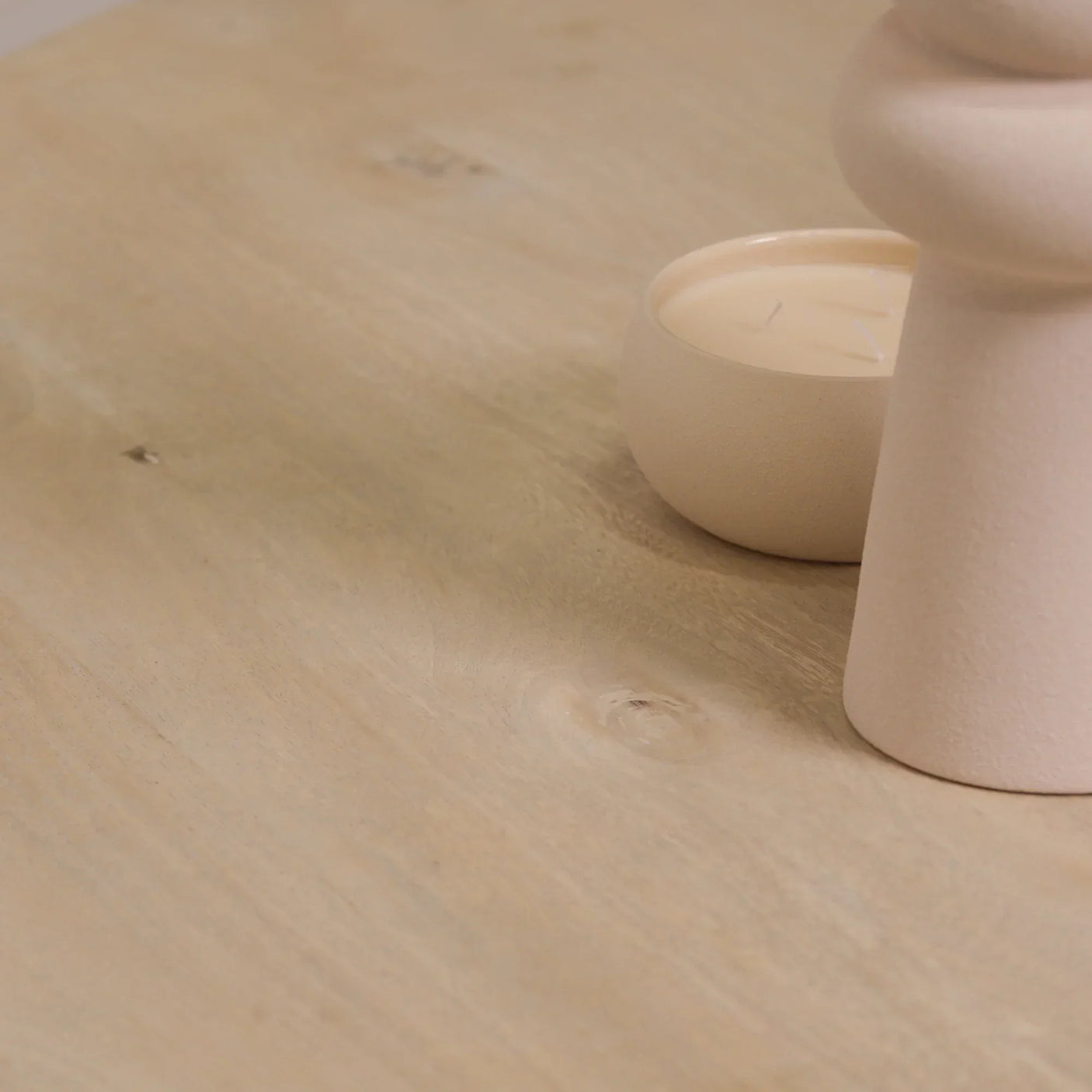 Light oak dining table surface with round beige candle and textured decor accent