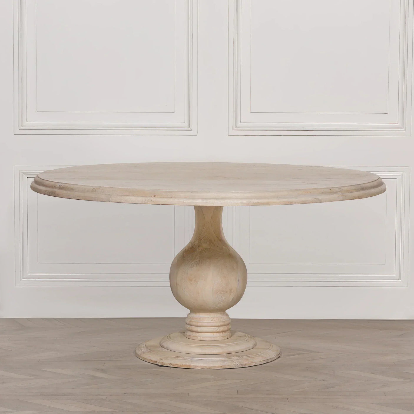 Round wooden dining table with pedestal base in light oak finish on herringbone floor