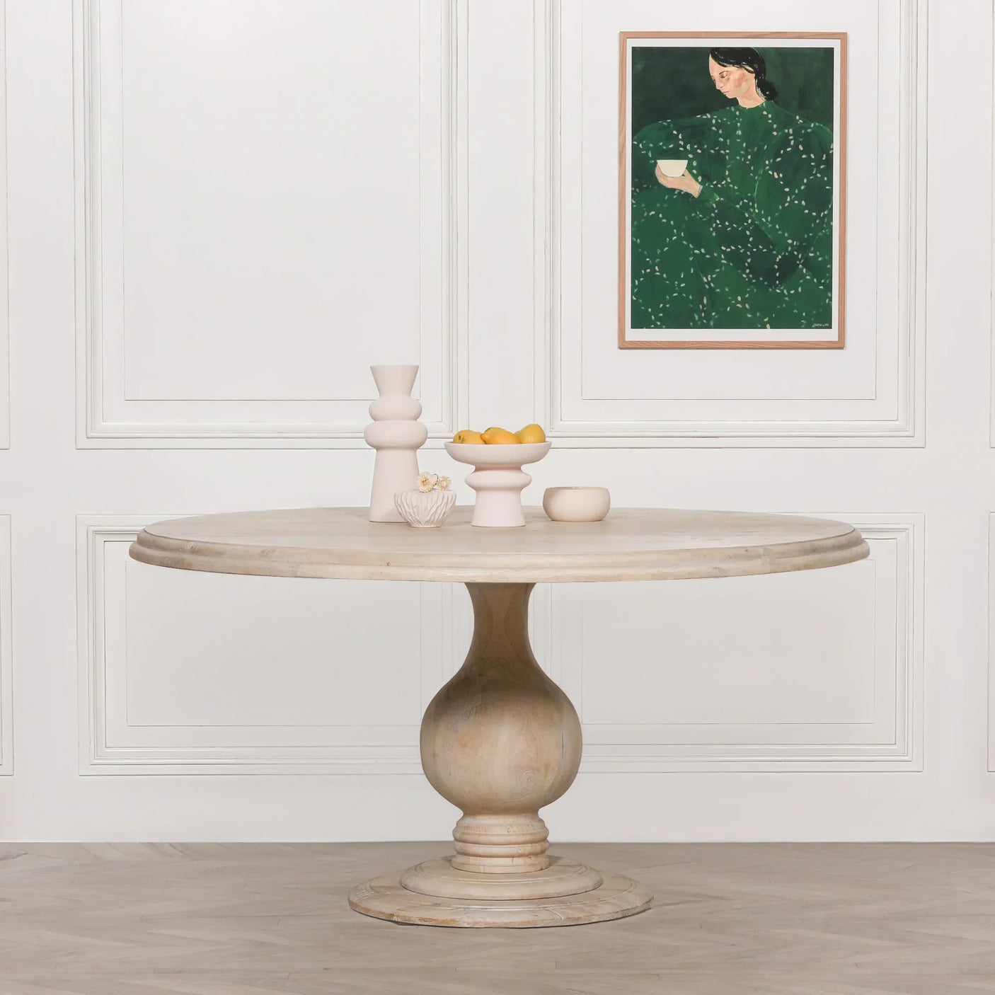 Round wooden dining table with pedestal base in light finish, styled with neutral decor