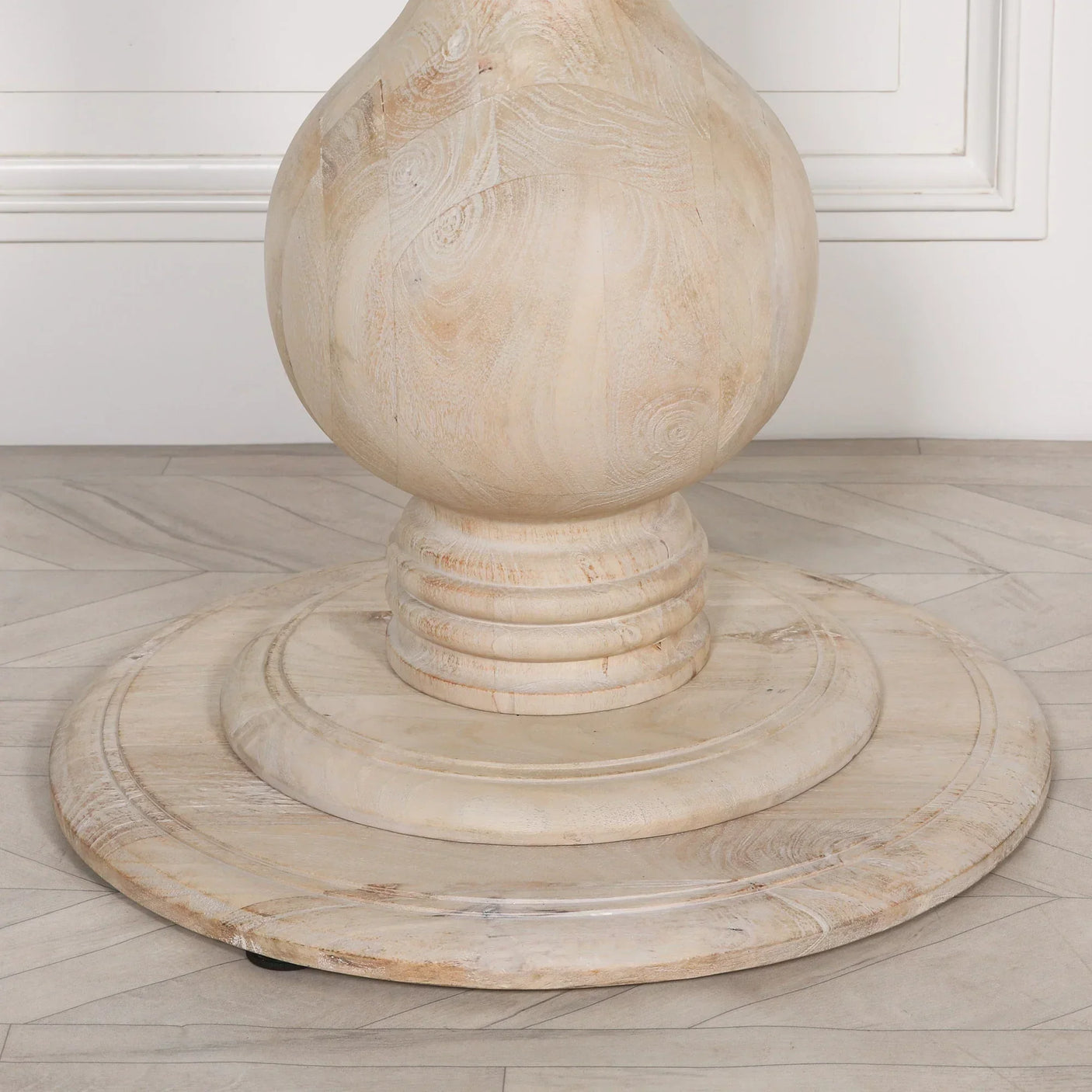 Round solid wood dining table base with natural finish on herringbone floor