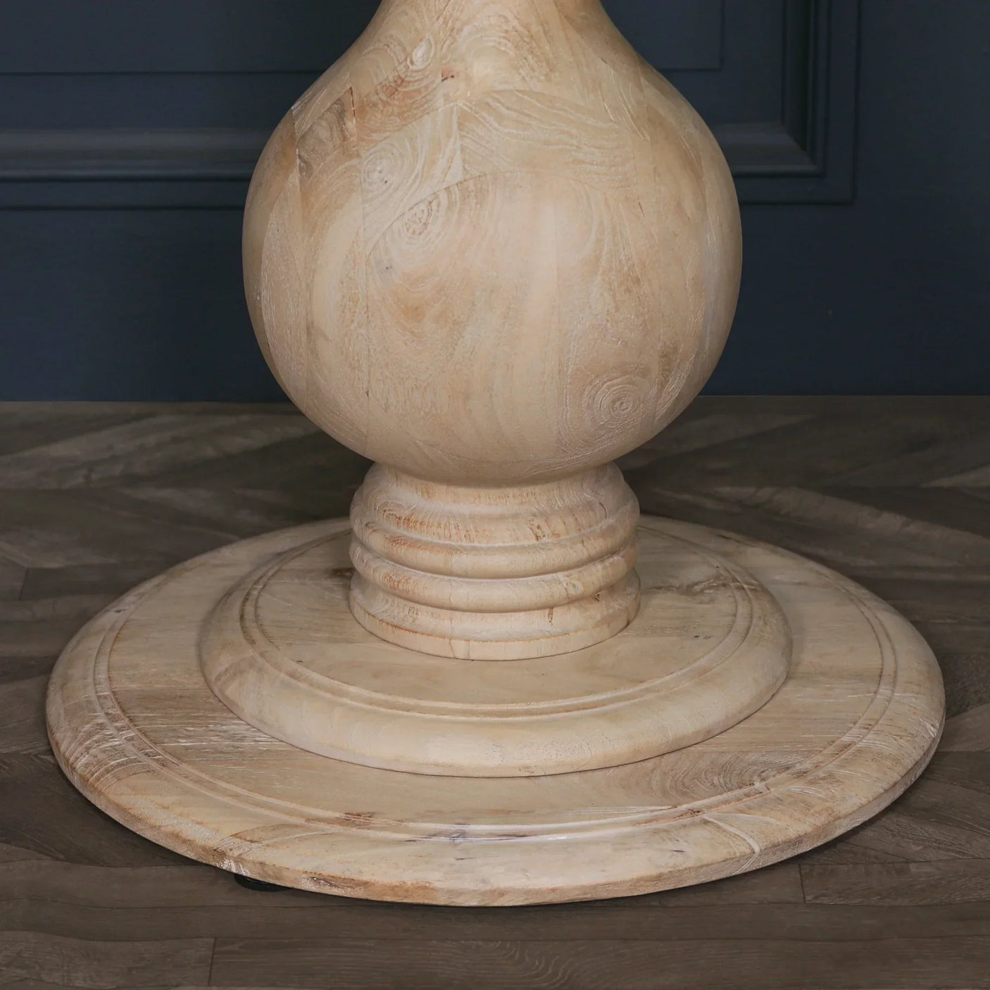 Round natural wood dining table pedestal base with carved details on wood floor