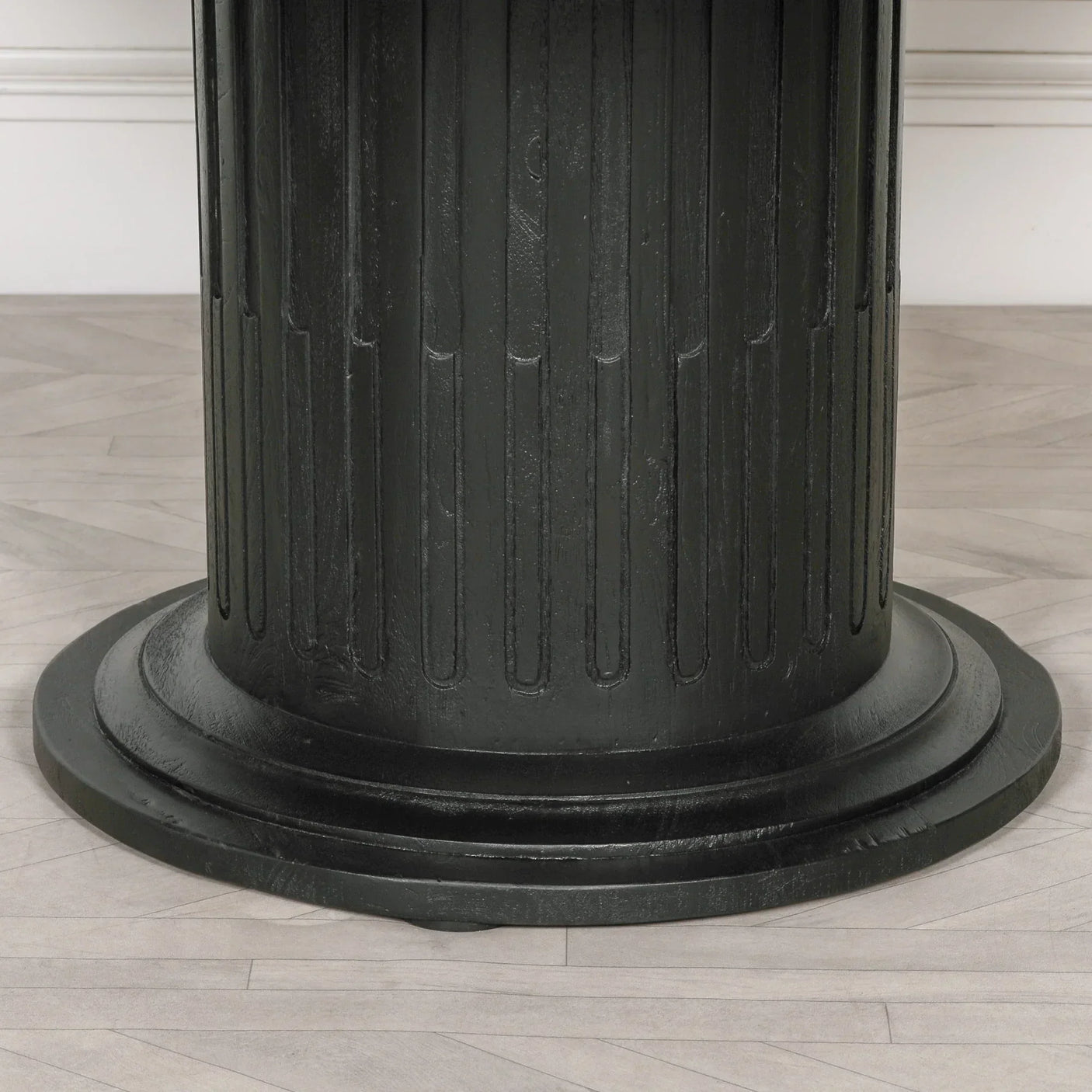 Black wood dining table pedestal base with vertical groove detail on light herringbone floor